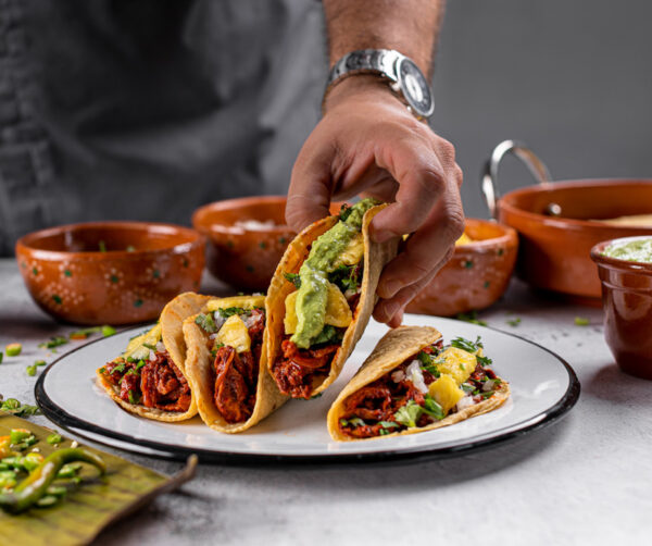 hand grabbing carne al pastor tacos with guacamole and pineapple