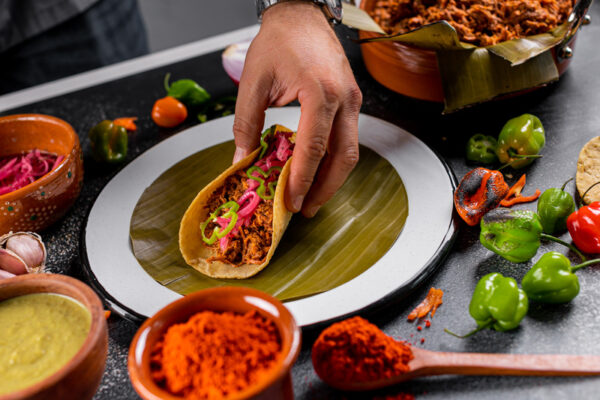 A hand grabbing a cochinita pibil taco with condiments